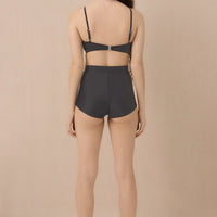 Woman wearing blueish grey high waist surf shorts, sustainable swimwear designed to stay on in the surf, offering supportive coverage and a flattering fit for active beach days.