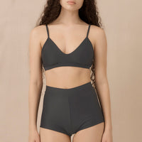 Woman wearing blueish grey high waist surf shorts, sustainable swimwear designed to stay on in the surf, offering supportive coverage and a flattering fit for active beach days.