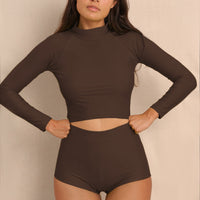 Woman wearing brown Aire Turtle Neck a high neck, minimalist long sleeve women’s rashguard made from sustainable fabric, designed for sun protection and surf performance.