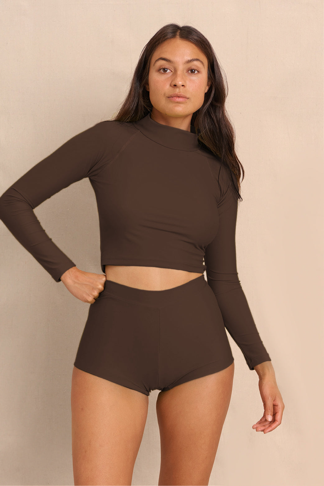 Woman wearing brown high waist surf shorts and matching rashguard, sustainable swimwear designed to stay on in the surf, offering supportive coverage and a flattering fit for active beach days.