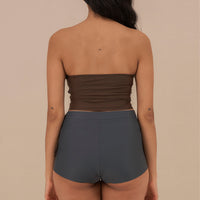 Woman wearing blueish grey high waist surf shorts, sustainable swimwear designed to stay on in the surf, offering supportive coverage and a flattering fit for active beach days.