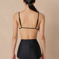 Woman wearing black high waist surf shorts, sustainable swimwear designed to stay on in the surf, offering supportive coverage and a flattering fit for active beach days.