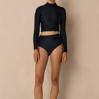 Woman wearing black Aire Turtle Neck a high neck, minimalist long sleeve women’s rashguard made from sustainable fabric, designed for sun protection and surf performance.
