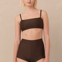 Woman wearing brown high waist surf shorts, sustainable swimwear designed to stay on in the surf, offering supportive coverage and a flattering fit for active beach days.