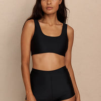 Woman wearing black high waist surf shorts, sustainable swimwear designed to stay on in the surf, offering supportive coverage and a flattering fit for active beach days.