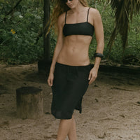 Woman in black bikini top and sheer black skirt standing on the beach