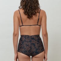 Woman wearing black and brown leaf print high waist surf shorts, sustainable swimwear designed to stay on in the surf, offering supportive coverage and a flattering fit for active beach days.